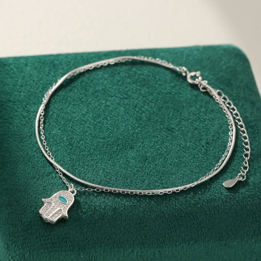 Bracelet de cheville double chaîne en argent 925 orné d'un pendentif Main de Fatma serti de petites pierres turquoise et blanches.