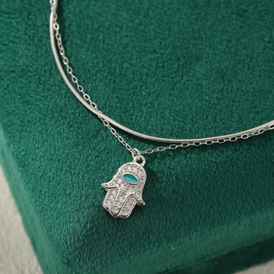 Bracelet de cheville double chaîne en argent 925 avec pendentif Main de Fatma orné de zircons blancs et d'une pierre bleue.