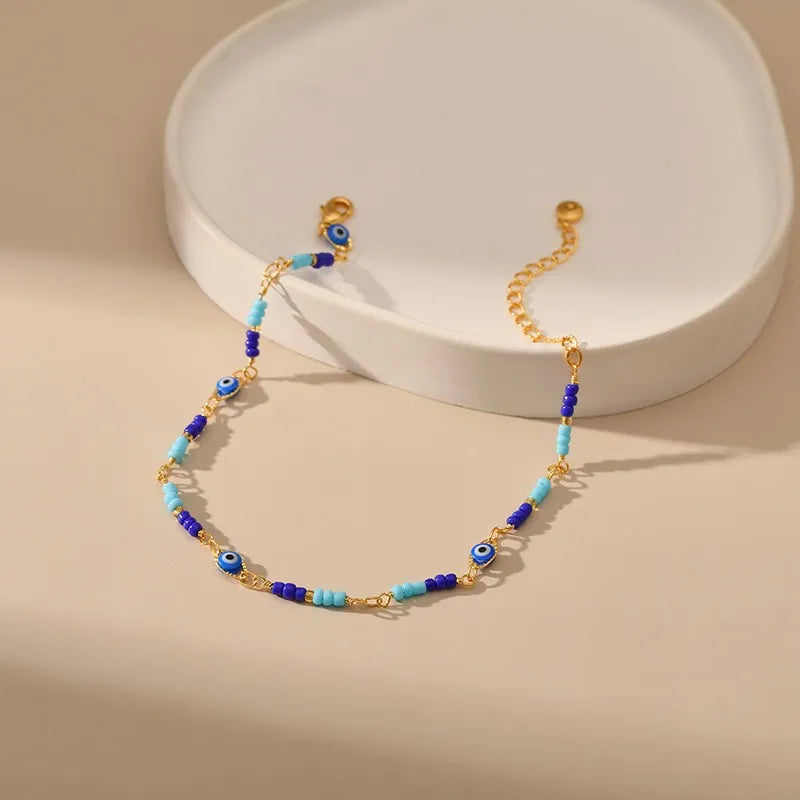 Bracelet de cheville doré avec des perles bleues et des breloques œil du mal pour la protection.