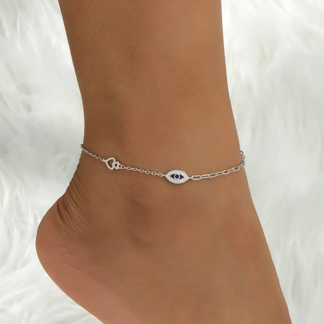 Bracelet de cheville en argent 925 orné d'un motif œil bleu et d'un petit cœur ajouré, porté à la cheville d'une femme.
