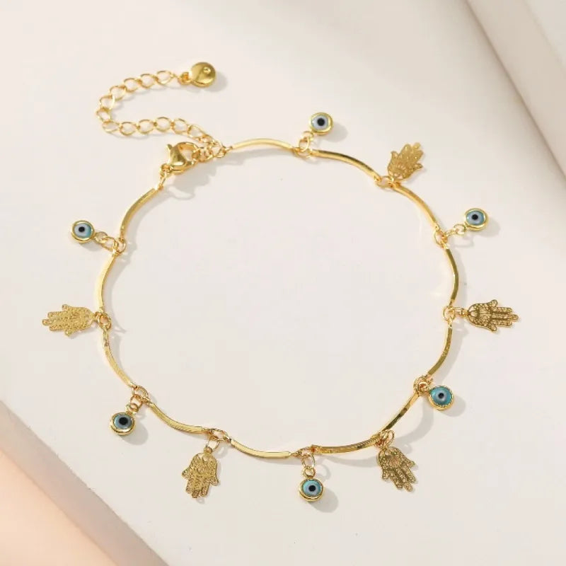 Bracelet de cheville doré avec plusieurs breloques : mains de Fatma stylisées et "mauvais œil" bleu et noir.
