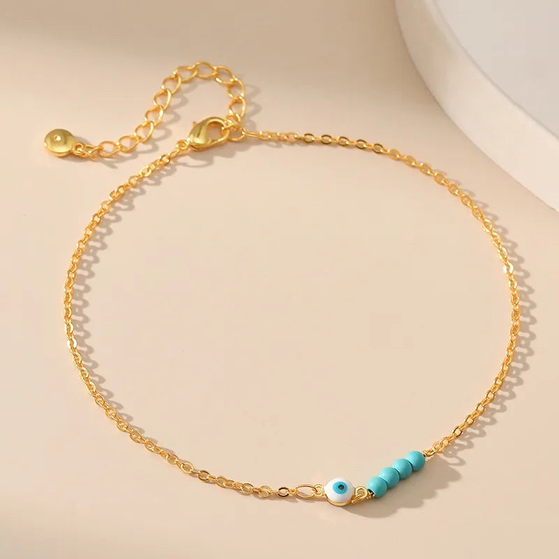 Bracelet de cheville doré avec une chaîne fine, orné d'un œil bleu et blanc et de petites perles turquoise.