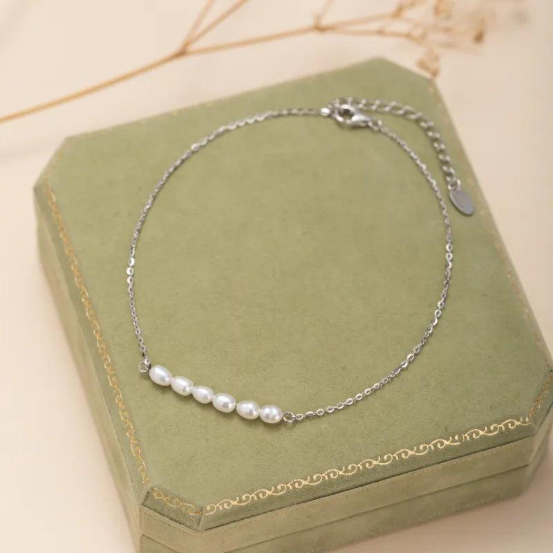 Bracelet de cheville en argent avec une chaîne fine ornée de cinq petites perles blanches disposées en ligne.