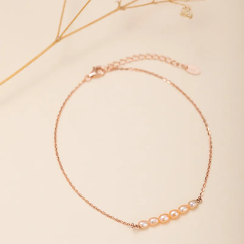 Bracelet de cheville en argent rosé avec sept petites perles couleur pêche disposées en arc sur une chaîne fine.