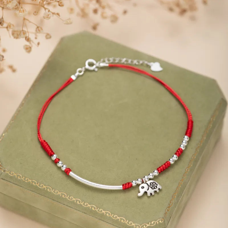 Bracelet de cheville "Petite Éléphant" en argent avec cordon rouge et perles argentées. Le bracelet est orné d'un charm éléphant stylisé avec une fleur.