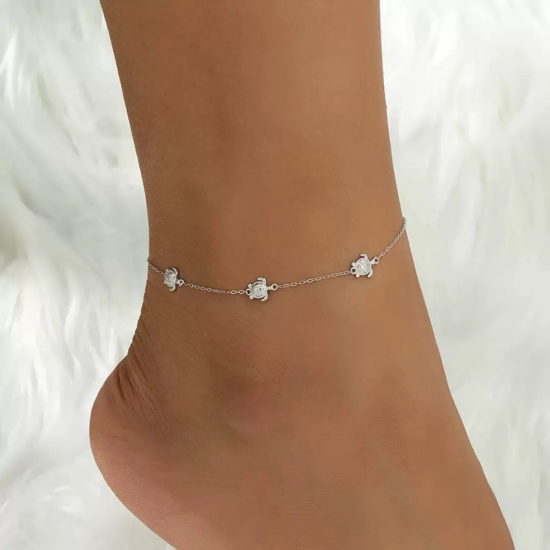 Bracelet de cheville en argent 925 orné de petites tortues marines délicates, porté sur une cheville féminine sur fond blanc.