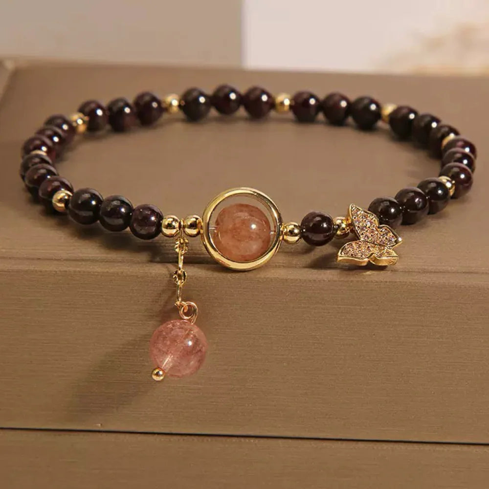 Bracelet en grenat et quartz fraise avec un pendentif papillon doré incrusté de zircons et une breloque ronde en quartz fraise, perles dorées entre chaque pierre.