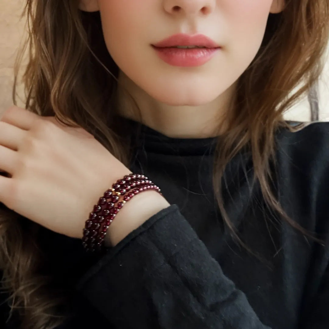 Bracelet Grenat "Passion" multi-rangs sur le poignet d'une femme, avec de petites perles rouge foncé et des accents dorés.