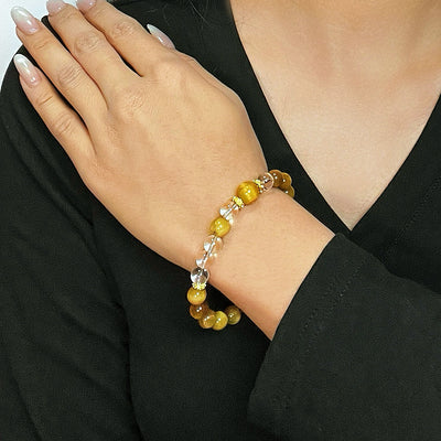 Bracelet en œil de tigre et cristal de roche "Énergie Vitale" porté au poignet d'une femme, montrant les perles dorées et transparentes alternées avec de petites perles dorées.