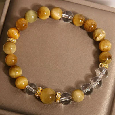 Bracelet fait de perles rondes œil de tigre dorées et de perles rondes en cristal de roche transparent, séparées par de petites perles dorées ornées de strass.