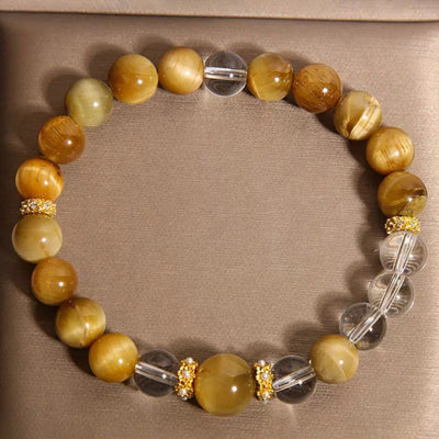 Bracelet "Énergie Vitale" fait main avec des perles d'œil de tigre dorées et des perles de cristal de roche transparentes, séparées par des ornements dorés incrustés de strass.