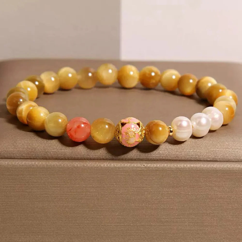 Bracelet élastique fait de perles d'œil de tigre dorées, alternant avec des perles d'eau douce blanches, des perles roses et une perle centrale rose sculptée avec des détails dorés.