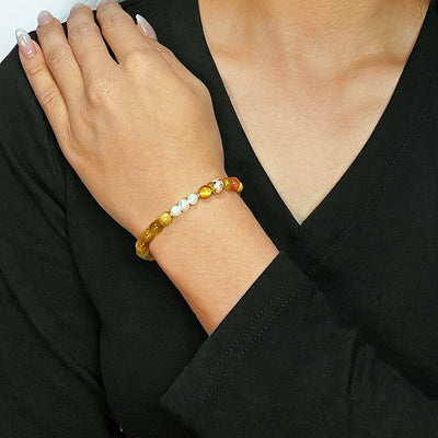 Bracelet "Élégance Discrète" en œil de tigre et perles blanches, porté au poignet d'une femme sur fond noir.