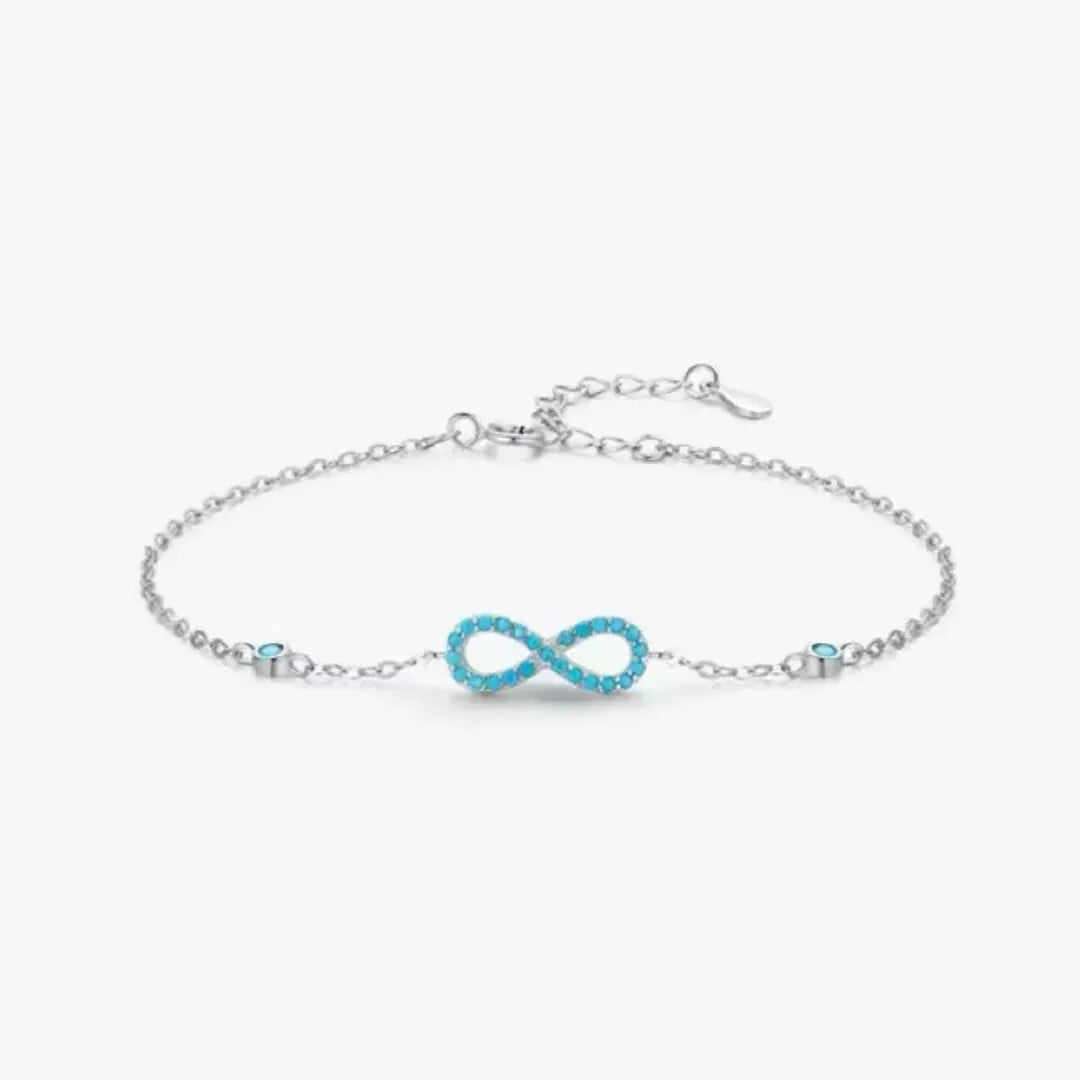Bracelet infini en argent 925 orné de petites pierres turquoise bleues. Le symbole de l'infini est délicatement serti de turquoises, avec deux autres petites turquoises discrètement placées sur la chaîne de chaque côté.