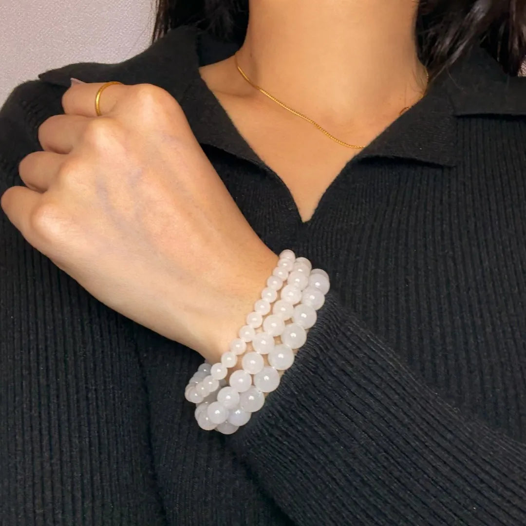 Trois bracelets en jade blanc "Douceur Blanche" de tailles différentes portés au poignet d'une femme sur un pull noir.