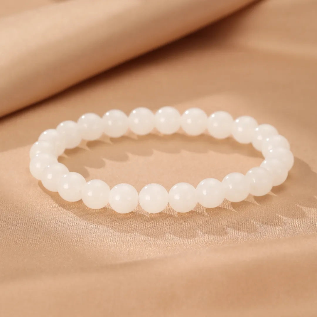 Bracelet "Douceur Blanche" en jade blanc, composé de perles rondes et lisses, posé sur un tissu satiné beige.