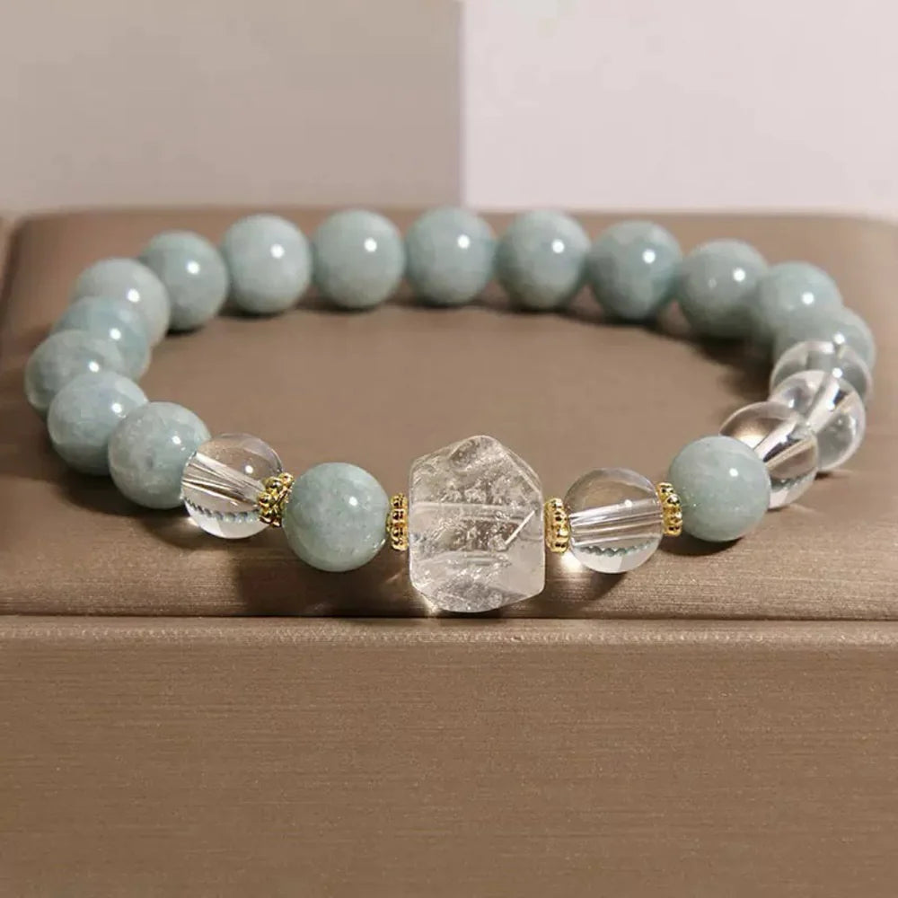 Bracelet "Clarté Apaisante" composé de perles de jade bleu pâle, de perles de cristal de roche facettées et d'une pierre centrale brute en cristal de roche, séparées par de petites perles dorées.