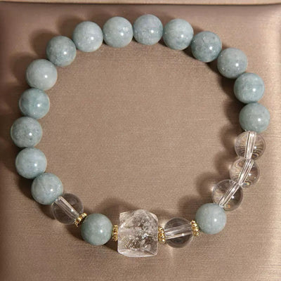Bracelet "Clarté Apaisante" fait de perles de jade bleu pâle et de cristal de roche, avec une pièce centrale brute de cristal de roche et des séparateurs dorés.