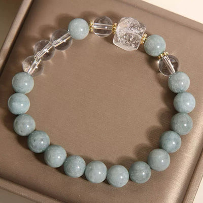 Bracelet "Clarté Apaisante" fait de perles rondes bleues pâles en jade et de perles transparentes en cristal de roche, avec une perle carrée centrale en cristal de roche légèrement texturée et des séparateurs dorés.