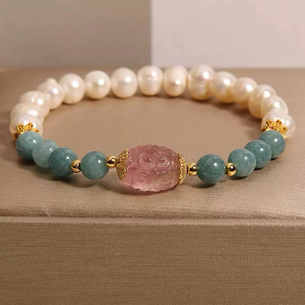 Bracelet fantaisie en perles de jade blanches, perles bleues d'aigue-marine et une pierre centrale sculptée rose, le tout rehaussé de petits éléments dorés.