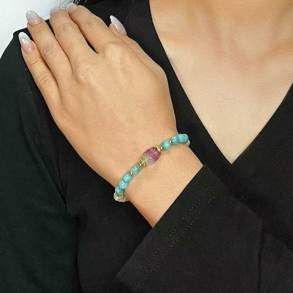 Bracelet "Pureté Naturelle" en perles de jade bleu ciel et fluorite rose, rehaussé de petites perles dorées, porté au poignet d'une femme.