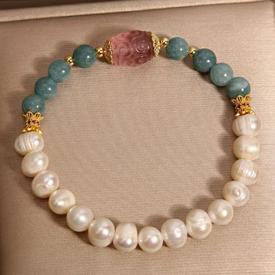 Bracelet orné de perles blanches nacrées, de perles rondes bleu sarcelle et d'une perle centrale sculptée rose, avec des accents dorés.