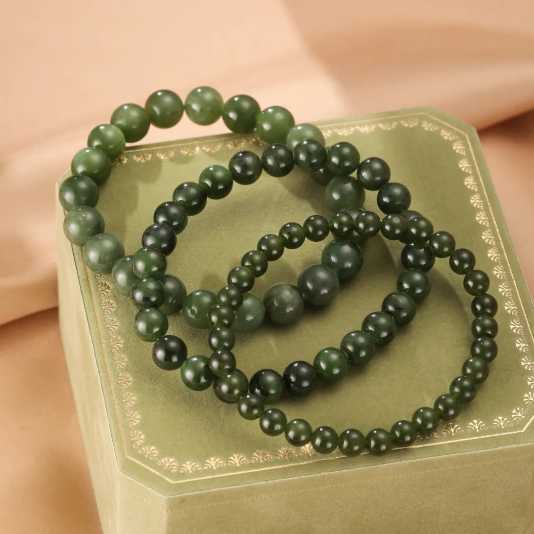 Trois bracelets en perles de jade vert de différentes tailles, posés sur un coffret vert orné d'une dorure délicate.
