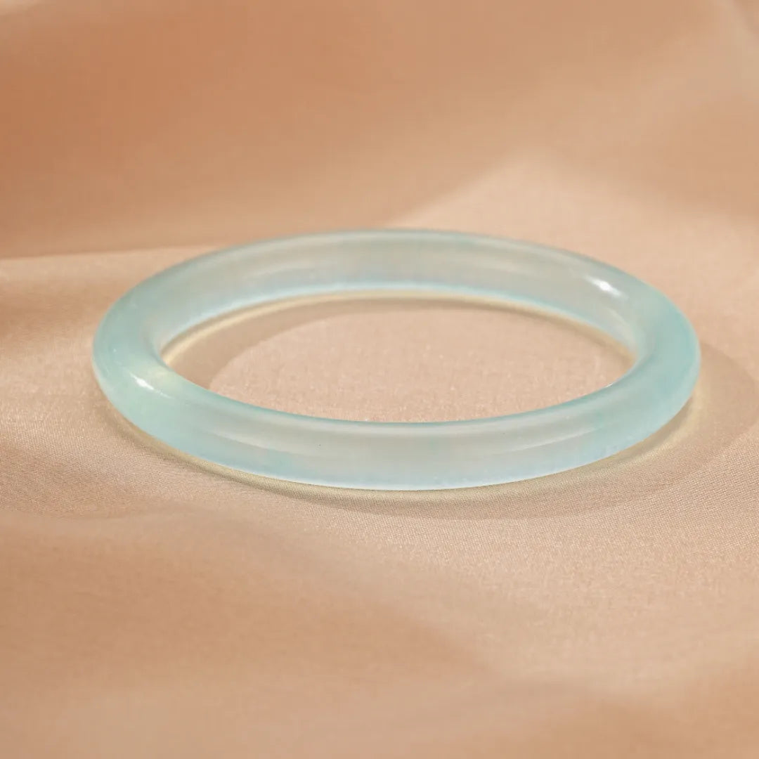 Bracelet jonc en aigue-marine "Douceur Marine" translucide et lisse sur fond beige satiné.