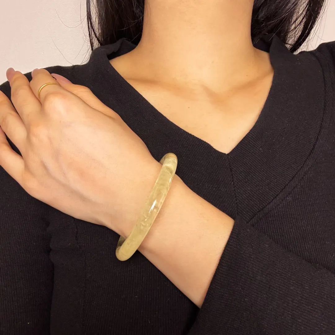 Bracelet jonc en citrine translucide "Reflets de Confiance" porté au poignet d'une femme sur un haut noir.
