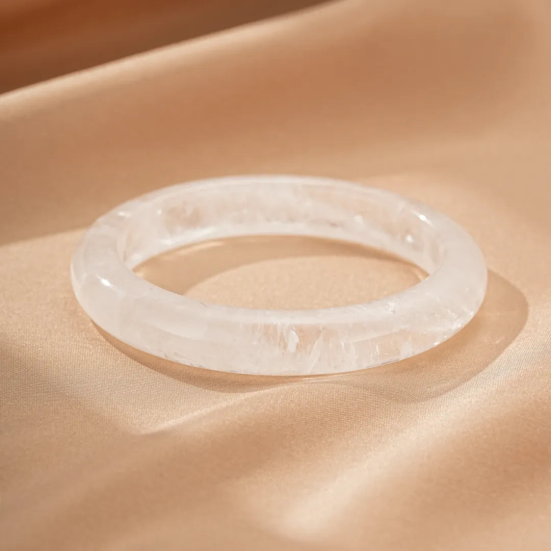 Bracelet jonc en cristal de roche translucide, monté sur un tissu satiné beige.
