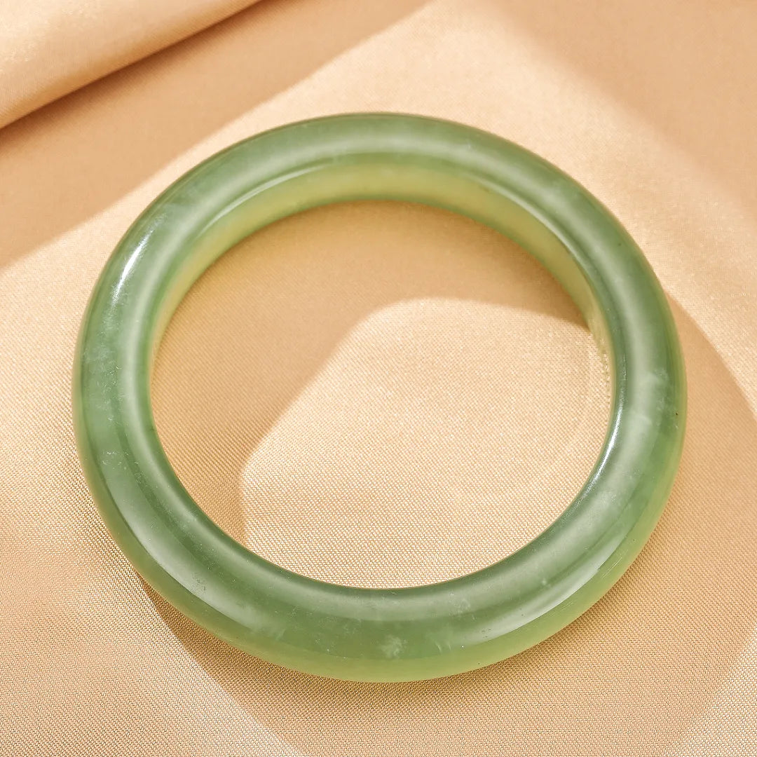 Bracelet jonc rond en jade vert clair, au design épuré, posé sur un fond beige.