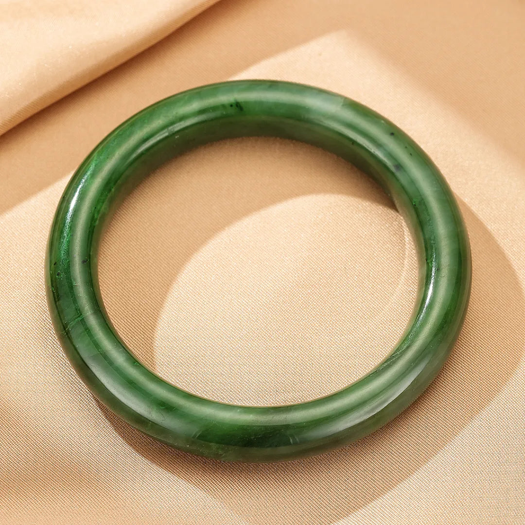 Bracelet jonc en jade de couleur verte profonde, poli et lisse, sur un fond beige satiné.