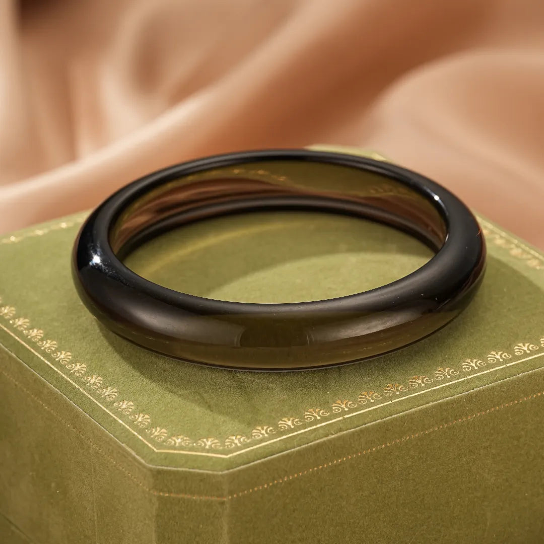 Bracelet jonc en obsidienne naturelle au fini poli, posé sur une boîte verte ornée de motifs dorés.