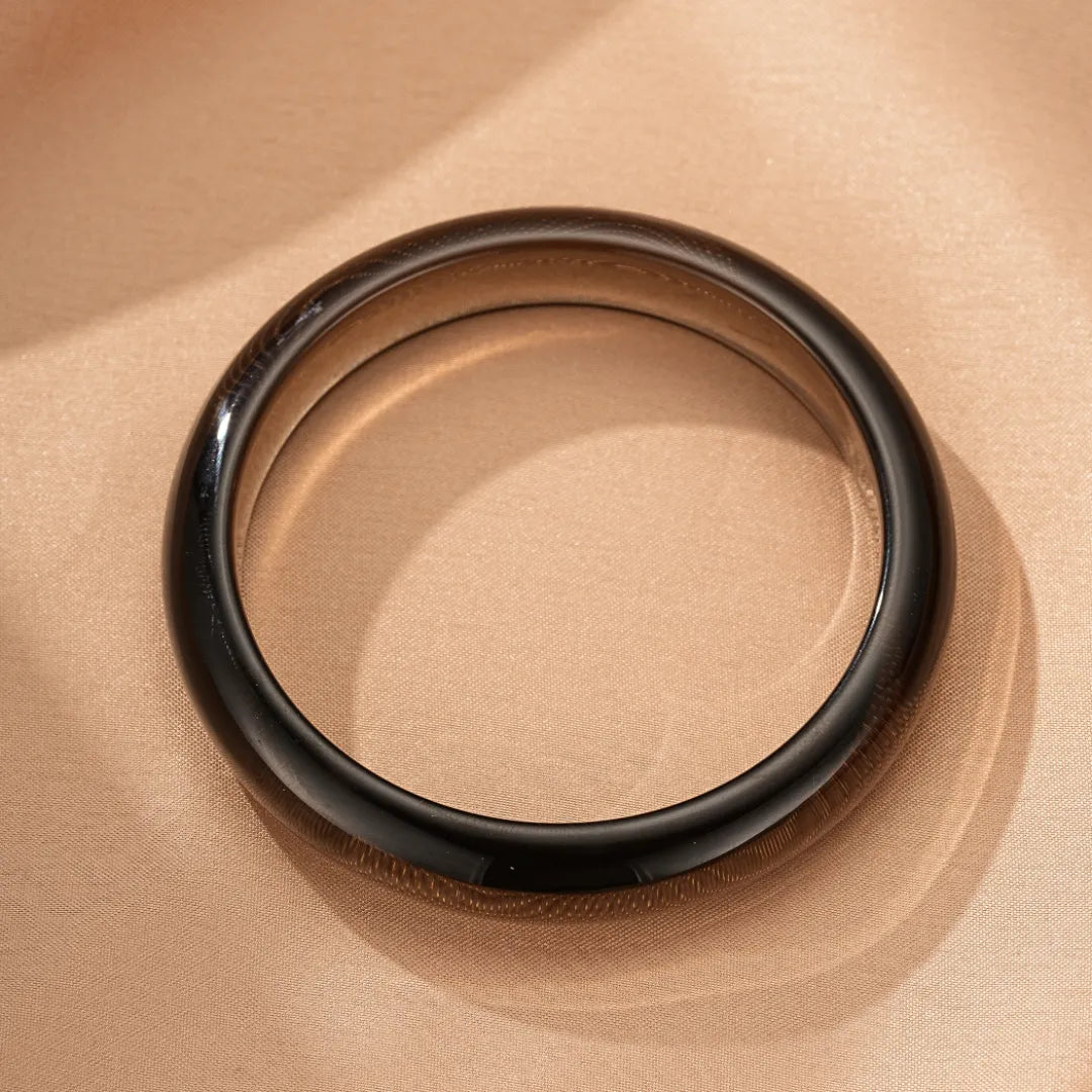 Bracelet jonc en obsidienne naturelle, forme ronde et polie, sur fond satiné beige.