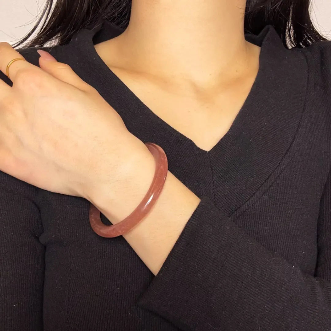 Bracelet jonc en quartz fraise, porté au poignet d'une femme, avec un design épuré et une couleur rose translucide.
