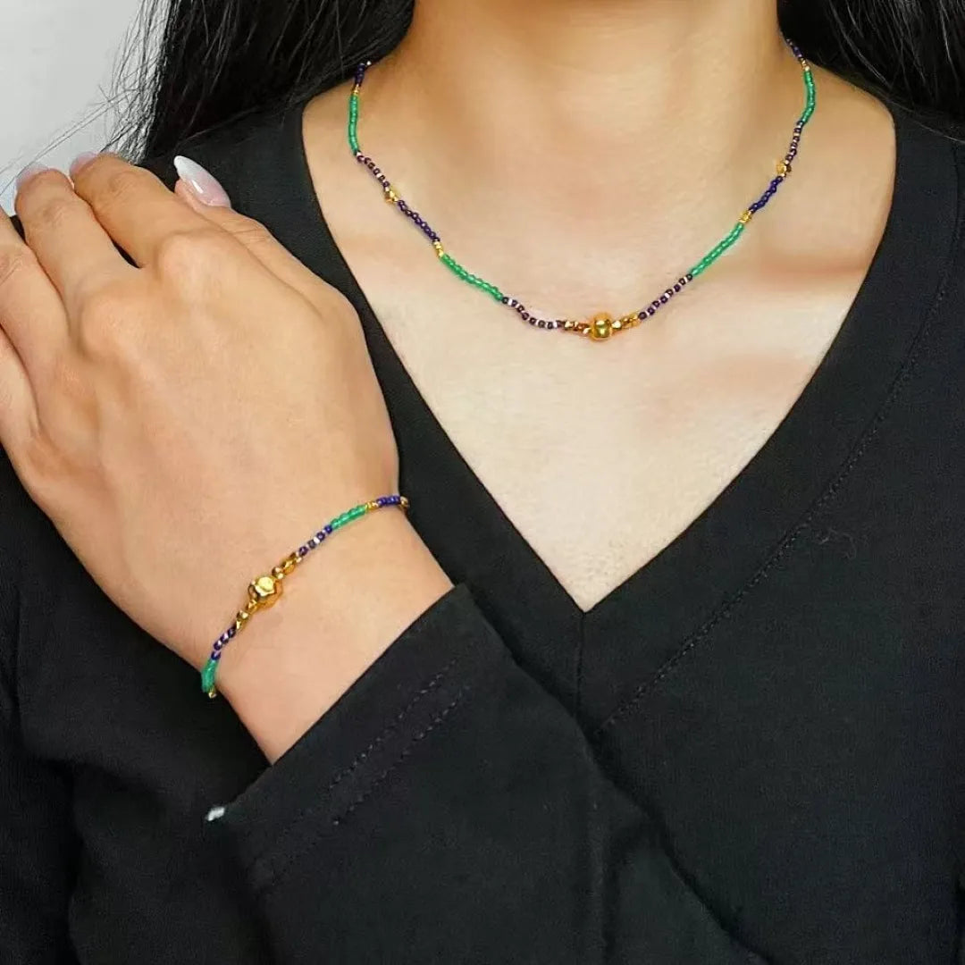 Ensemble bracelet et collier de perles fines vertes, bleues et dorées, avec une perle centrale dorée sur le collier et un fermoir doré sur le bracelet.