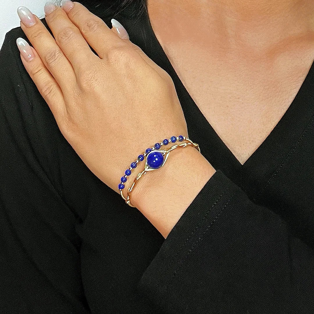 Bracelet double rang en lapis lazuli avec une pierre bleue centrale en forme d'œil, monté sur un fil doré torsadé, porté au poignet d'une femme.