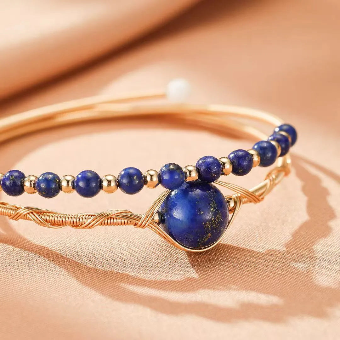 Bracelet avec un gros pendentif en lapis-lazuli bleu profond et des petites perles bleues et dorées, monté sur un fil doré torsadé.
