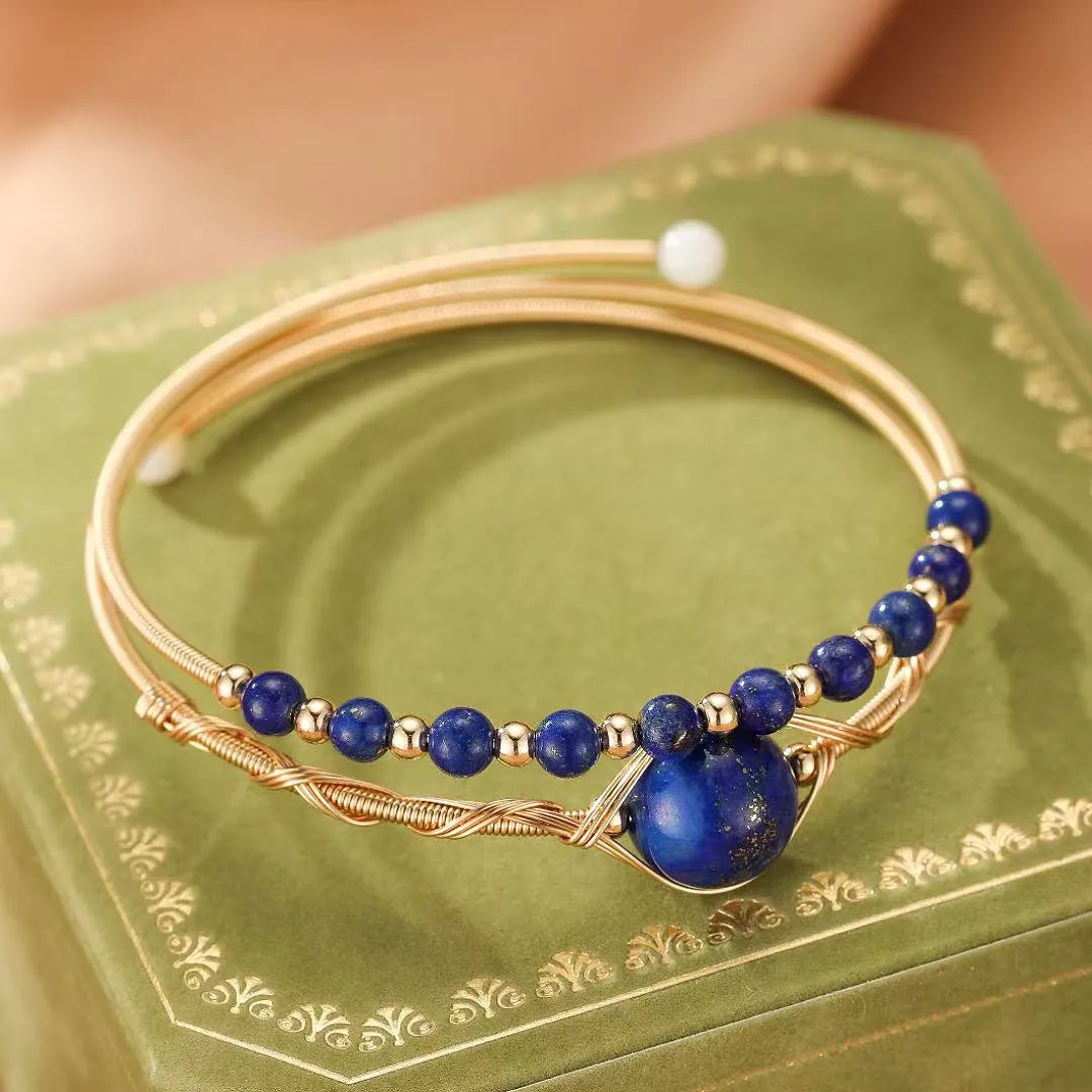 Bracelet jonc doré orné de perles de lapis-lazuli et d'une grosse perle centrale, avec un design torsadé délicat.