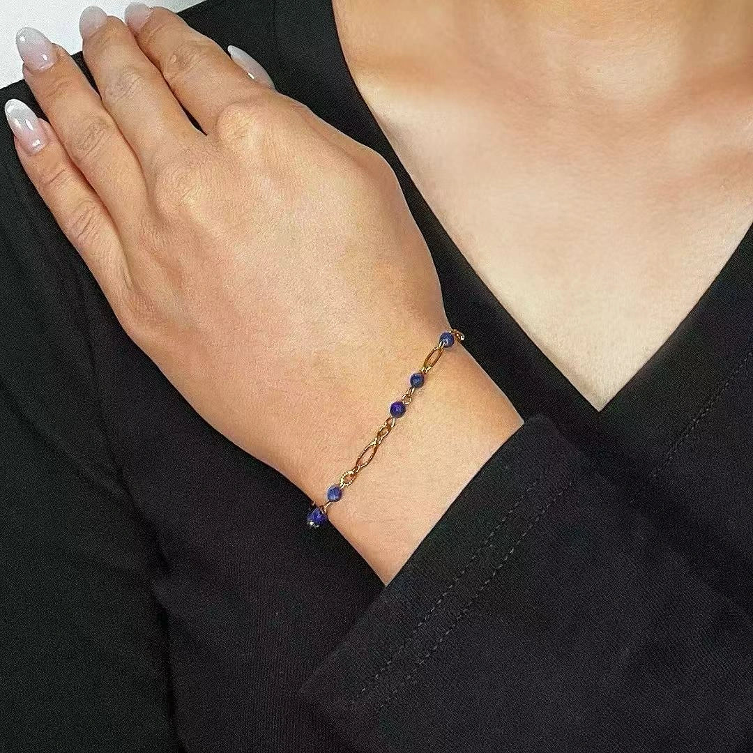 Bracelet Lapis Lazuli "Reflets Étoilés" avec des petites perles bleues et une chaîne dorée porté au poignet d'une femme.