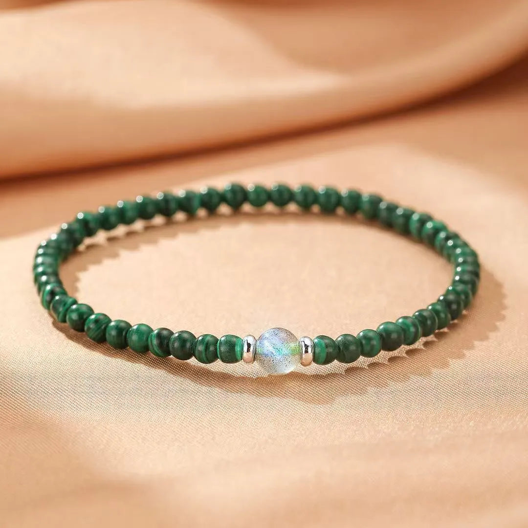 Bracelet fait de perles de malachite verte et d'une perle centrale de labradorite irisée, avec des séparateurs en argent. Le bracelet est nommé "Transformation Intérieure".