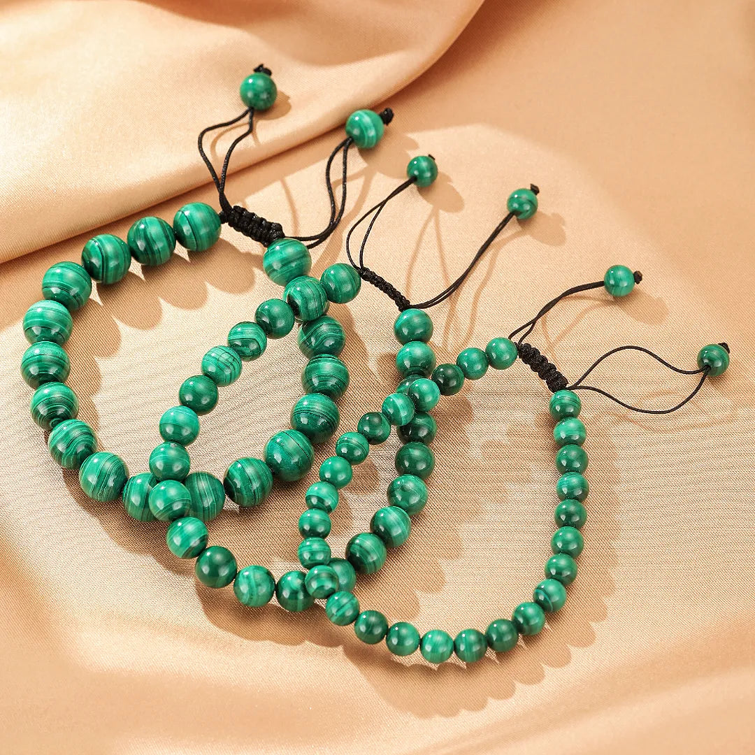Trois bracelets ajustables en pierres naturelles de malachite verte, avec des perles de différentes tailles, sur un fond beige satiné.