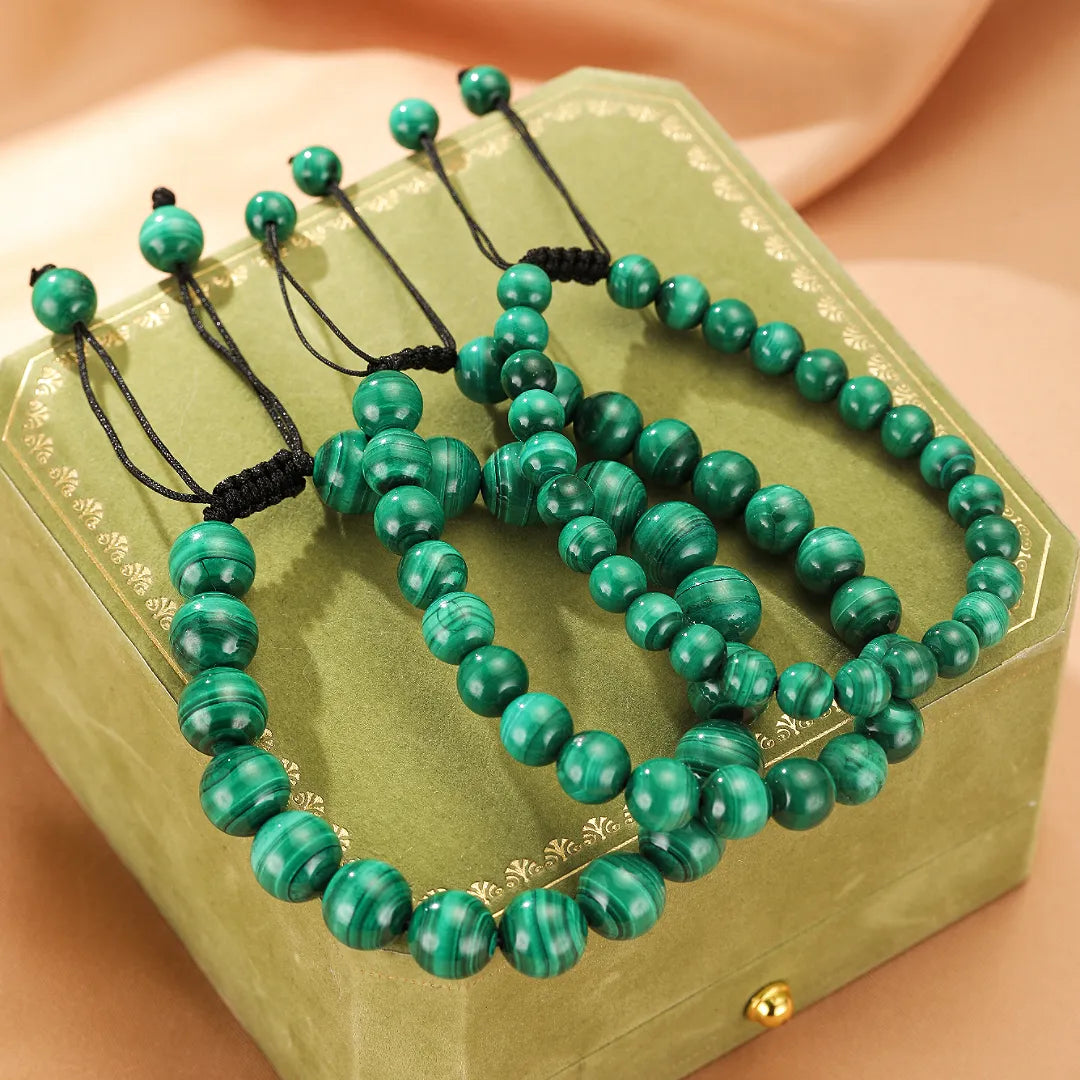 Trois bracelets en pierres naturelles de malachite verte, avec des perles de différentes tailles, posés sur un coffret vert.