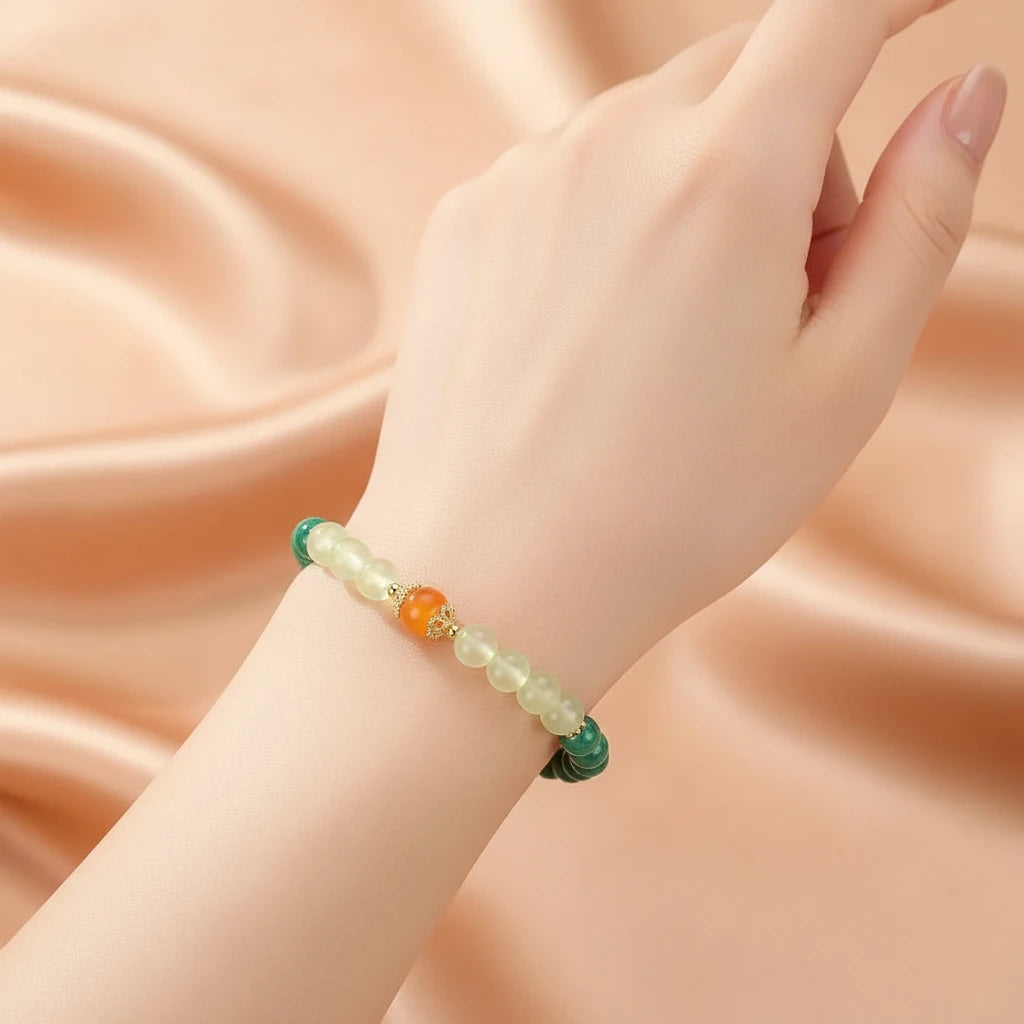 Bracelet "Harmonie Colorée" en malachite, préhnite et ambre, porté au poignet d'une femme sur un fond satiné pêche.