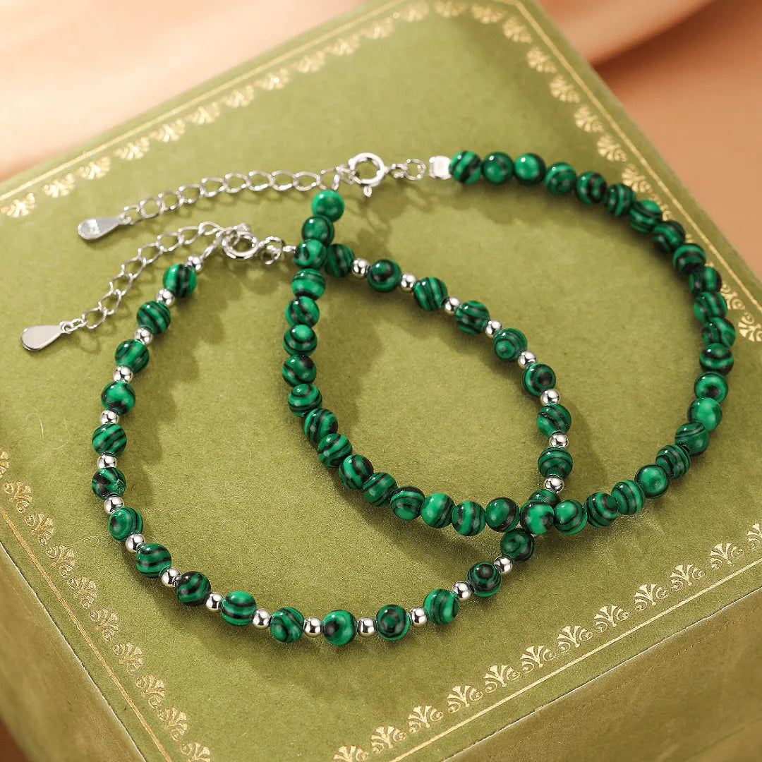 Deux bracelets en malachite "Veines d'Harmonie" avec des perles en argent, sur un fond vert.