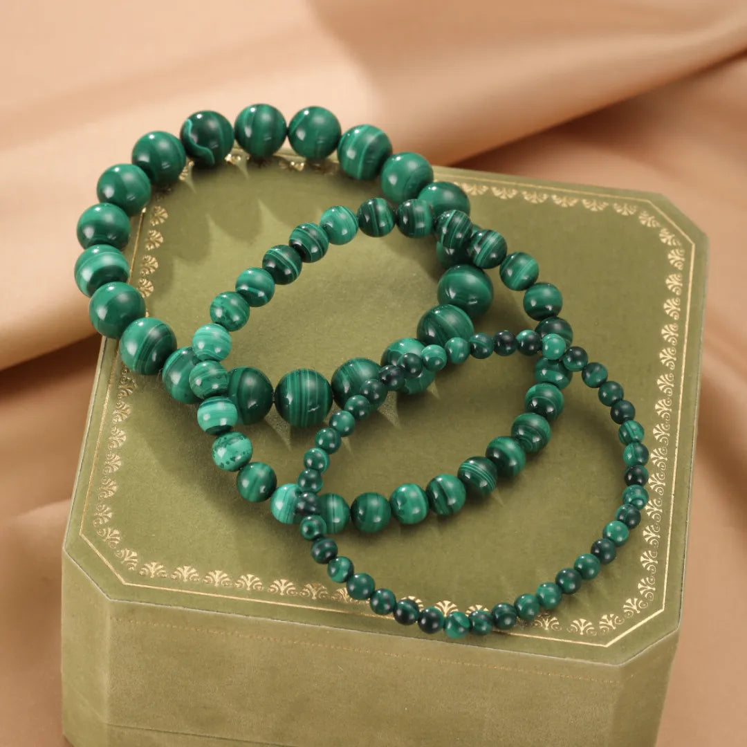 Trois bracelets en perles de malachite verte aux veines caractéristiques, posés sur une boîte verte ornée.