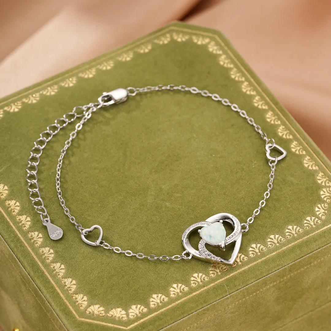 Bracelet en argent avec un pendentif en forme de cœur orné d'une opale et de petites pierres scintillantes, avec des cœurs plus petits le long de la chaîne.