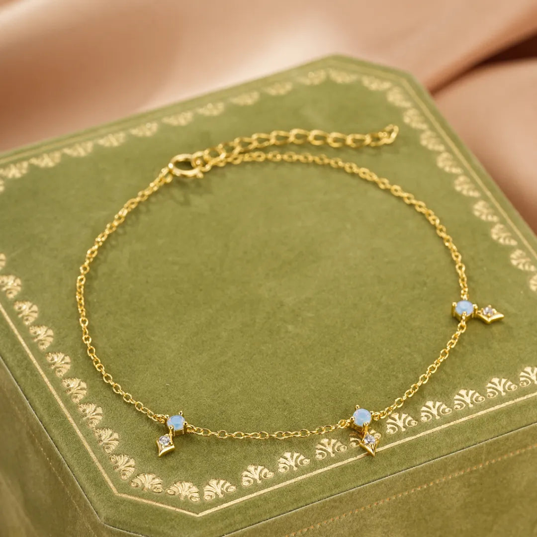 Bracelet fin en argent doré or, orné de petites pierres opales bleues et de pendentifs en forme de losange sertis de cristaux.
