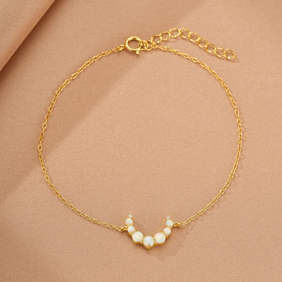 Bracelet fin en argent doré 18 carats avec un pendentif en forme de croissant de lune orné d'opales et de petits diamants.