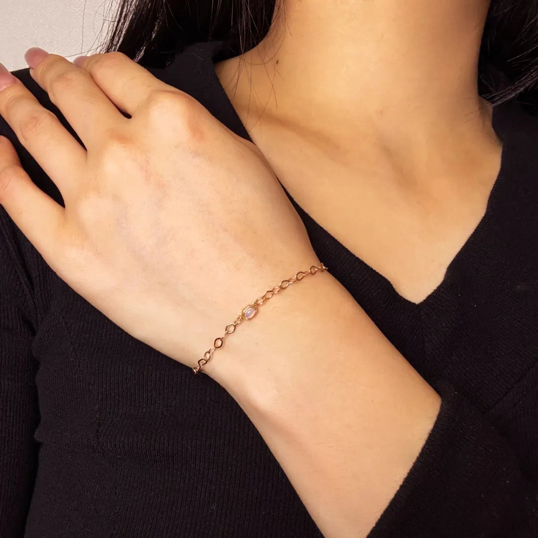 Bracelet fin en argent doré or avec une petite pierre opale centrale, porté au poignet d'une femme.